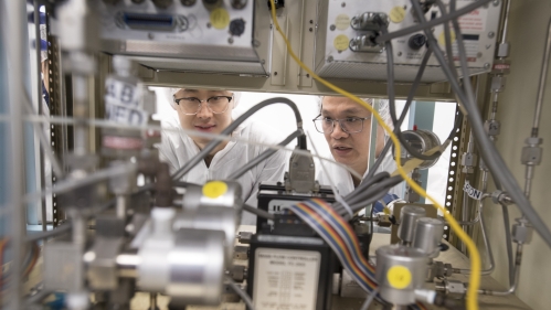 Two Asian males work in clean room laboratory environment.