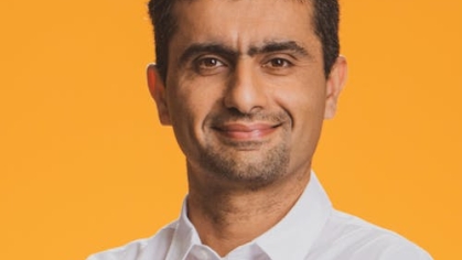 Headshot of man with black hair and white open collared shirt.