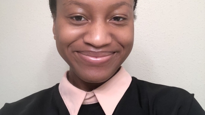 Head shot of female African American undergraduate student, smiling wearing a pink blouse under a black sweater. Her hair is parted in the middle and tied back.