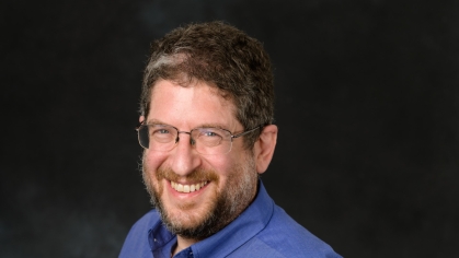 Head shot of male with glasses and beard wearing a blue button down shirt.
