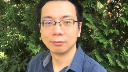 Head shot of Asian male with short black hair and eyeglasses wearing a blue button down shirt.