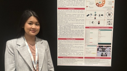 Young Asian female student standing next to her poster at a conference.