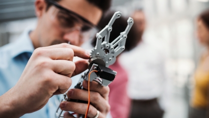 A young man working with robotic hand standing in lab.