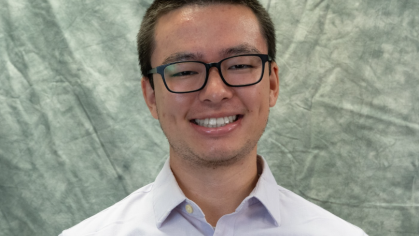 Headshot of Asian male with short black hair, wearing black horn rimmed, and light colored button down shirt. 