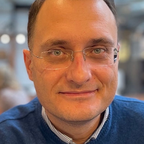 Head shot of male with short brown hair with eyeglasses wearing a blue pullover sweater.
