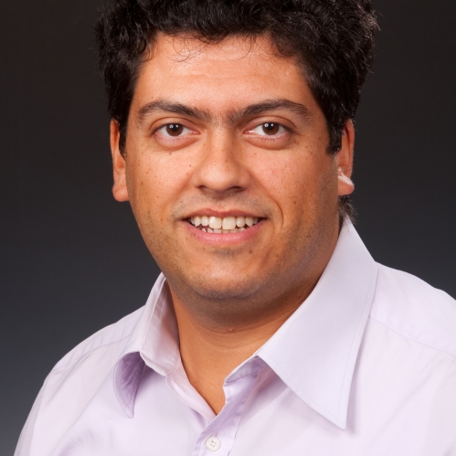 Head shot of male with curly, short, brown hair wearing a button down shirt.