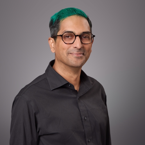 Headshot of male with green hair and eyeglasses wearing a dark button down shirt.