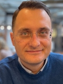 Head shot of male with short brown hair with eyeglasses wearing a blue pullover sweater.