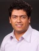 Head shot of male with curly, short, brown hair wearing a button down shirt.