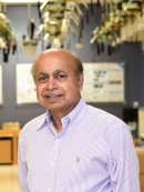 Head shot of balding Indian male wearing a pale button down shirt.