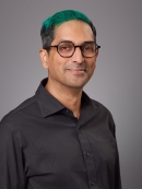 Headshot of male with green hair and eyeglasses wearing a dark button down shirt.
