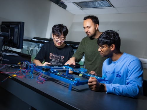 Two male students are receiving instructing from a male professor in a laboratory setting.