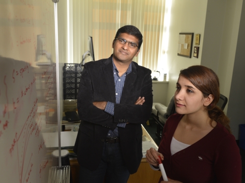 Male professor with crossed arms instructing a female student in front of a white board.