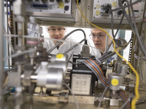 Two Asian males work in clean room laboratory environment.