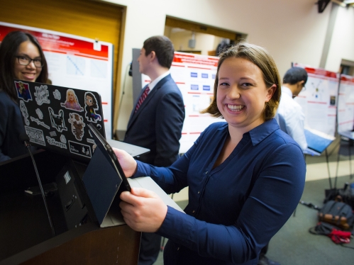 Smiling female student standing in front of a laptop.