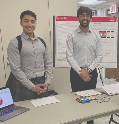 Two male students stand behind a table.
