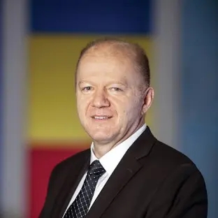 Headshot of a man with close cropped hair wearing a black suit and tie and white shirt.