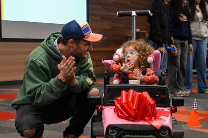 Kevin Groff with his daughter Zora, who is riding a pink car toy that Rutgers students redesigned for her.