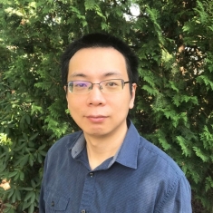 Head shot of Asian male with short black hair and eyeglasses wearing a blue button down shirt.
