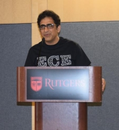 Male with black curly hair with eyeglasses standing behind a podium wearing an ECE black t shirt.